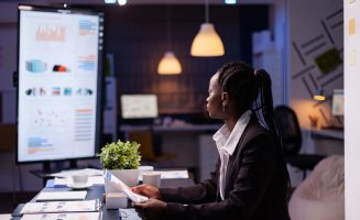 Focused workaholic african american businesswoman working at company financial charts presentation late at night in meeting office room. Overworked manager with dark skin checking profit statistics